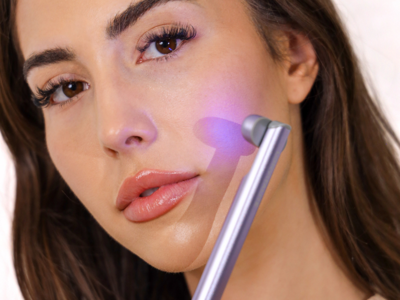 A woman treating her face with the LONVITALITE PRO LED Facial Wand using blue light therapy
